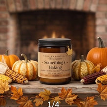 A candle jar labeled 'Something's Baking' by Rod Essentials Home Collection, styled on a rustic wooden surface with pumpkins, corn, autumn leaves, and a blurred fireplace background. Text overlay reads '1/4 FALL IN LOVE WITH HOME'.