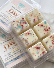 Six square wax melts in a clear plastic clamshell package with printed cards behind them. The wax is creamy off-white with scattered red, blue, and tan sprinkles.