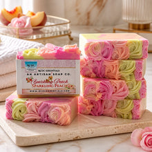 A bar of handmade cold process goat's milk soap with pink and yellow layers, decorated with a floral design, next to a vase with peach flowers.