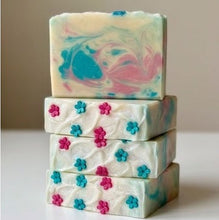 Four stacked handmade soap bars with a marbled pattern of pink, blue, and cream swirls, decorated with small 3D flower embellishments on the side bars, set against a neutral beige background.