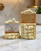 Two artisan lemon poppy soap bars on a white marble surface. One bar is wrapped in a paper label showing the brand 'Redc Essentials' and the scent 'Lemon Poppy'.