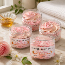 Jars of pink rose and orange blossom honey whipped soap scrub with a plant and flowers in the background.