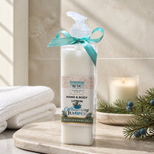 Hand and body lotion bottle with a teal ribbon on a bathroom counter with towels and a candle in the background.