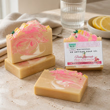 A image of handmade Pink Lemonade soap with pink and yellow colors, decorated with lemon slice designs, displayed with white towel and other decorative items.