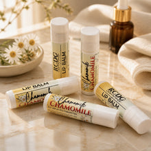 Lip balms with chamomile flavor on a wooden surface with flowers and a towel in the background.