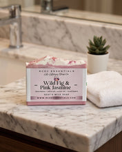 A bar of RCDC Essentials Wild Fig & Pink Jasmine goat milk soap sits on a white marble bathroom counter next to a folded white towel and a small potted succulent.