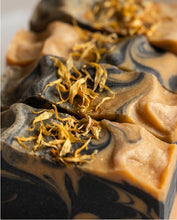 Close-up of handmade marbled soap bars in warm tan and dark charcoal swirls, topped with dried yellow flower petals.