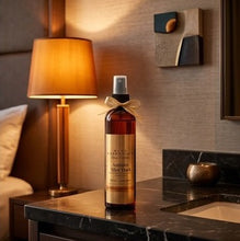 A bottle of Aged 15 Year Single Malts whisky by Macallan St. George's, styled on a dark marble countertop in a warm, modern hotel or home bar setting with a lit table lamp and textured wall.