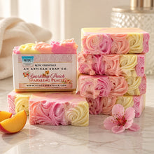 A bar of handmade cold process goat's milk soap with pink and yellow layers, decorated with a floral design, next to a vase with peach flowers.
