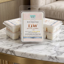 A clear plastic clamshell package of RDG Essentials DW Hotel Lobby scented melting wax tarts sits on a marble-topped table, with stacked wax tarts and a cream upholstered sofa in the background.