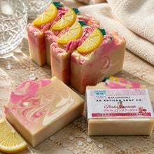 A image of handmade Pink Lemonade soap with pink and yellow colors, decorated with lemon slice designs, displayed with white towel and other decorative items.