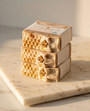 Three stacked bars of honey-infused soap on a white marble slab, featuring a textured honeycomb pattern and a gold bee detail, with a label reading 'HONEY BEE MANCHEST'.