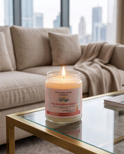 A lit jar candle sits on a glass coffee table in front of a beige sofa with a blurred city skyline in the background. The candle label reads 'Signature Journe Collection' and 'The Grounding Effect'.