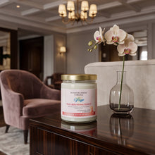 A jar candle labeled 'Signature Scents' and 'The Golden Hour Effect' sits on a polished dark wood console table in a luxurious room setting, next to a glass vase holding a single pale orchid.