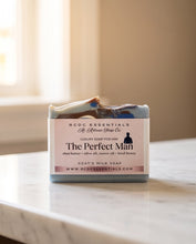 A bar of marbled soap labeled 'The Perfect Man' by RCDC Essentials, set on a white marble countertop with a softly blurred beige background.