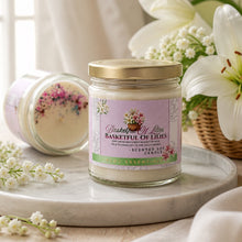 Scented soy candle labeled 'Basketwork of Lilies' on a marble surface with flowers in the background