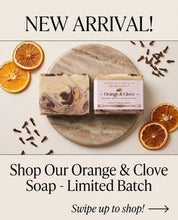 Two bars of soap labeled 'Orange & Clove' by Rose Essentials are displayed on a round stone tray with dried orange slices and cloves around them, under a 'NEW ARRIVAL!' banner and the text 'Shop Our Orange & Clove Soap - Limited Batch'.