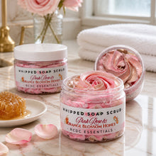 Jars of pink rose and orange blossom honey whipped soap scrub with a plant and flowers in the background.