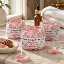 Jars of pink rose and orange blossom honey whipped soap scrub with a plant and flowers in the background.