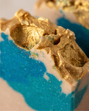 Close-up of a decorative bar with a textured gold foil top and a bright blue glittery lower section, set against a softly blurred light background.