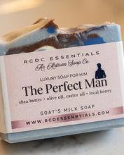 A close-up of a handmade soap bar with a pink paper label reading 'RCDC ESSENTIALS The Perfect Man' on a light marble surface.