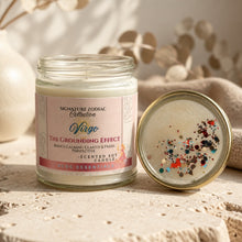 A glass jar candle labeled 'Signature Zodiac Collection' and 'The Grounding Effect' sits on a textured stone surface next to its lid, which is open to reveal multicolored glitter inside. The background features soft beige bokeh and dried botanical elements.