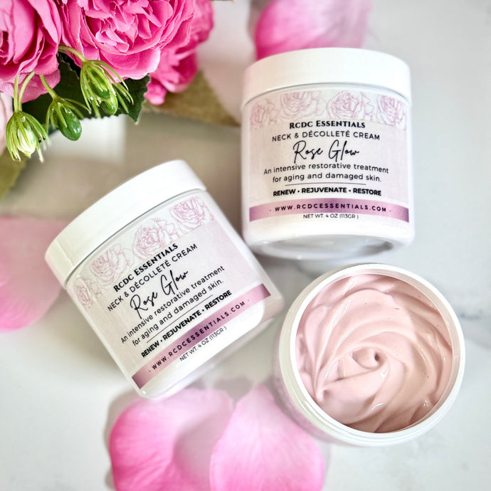 Two jars of RCDC Essentials Neck & Décolleté Cream with pink flowers and petals on a light background.
