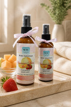 Two bottles of RDC Essentials Summer Melon Bliss fragrance body mist on a wooden surface with fruits and a plant in the background.