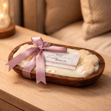 Candle in a wooden bowl with a pink ribbon on a wooden surface