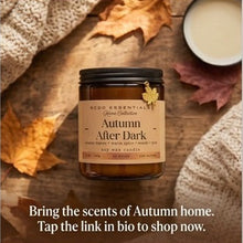 A jar candle labeled 'Autumn After Dark' by KCOO ESSENTIALS, shown in a cozy autumn flat-lay with fall leaves, a knit sweater, and a cup of coffee. Text below says, 'Bring the scents of Autumn home.