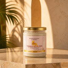 A glass jar candle with a gold lid and a cream label reading 'Signature Zodiac Collection Leo Summer Never Ends' sits on a warm beige stone surface with soft sunlight and leaf shadows in the background.
