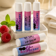 Lip balms with raspberry flavor on a light surface with raspberries and mint leaves.