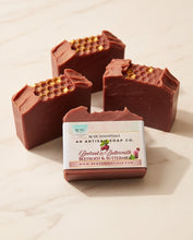 Four handmade beetroot and butterclove soap bars arranged on a light marble surface, with one bar in front showing the product label. The soaps are reddish brown with gold honeycomb details on top.