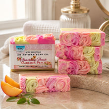 A bar of handmade cold process goat's milk soap with pink and yellow layers, decorated with a floral design, next to a vase with peach flowers.