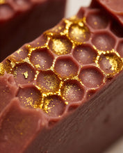 Close-up of a honeycomb-patterned bar, likely soap, in a deep berry purple with shimmering gold foil accents.