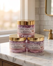 Three jars of Woodstock Whipped Soap Scrub stacked on a marble countertop in a bright bathroom setting.