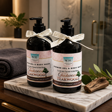 Two bottles of RCDC Teakwood shower gel and body wash on a marble tray with a blurred bathroom background.