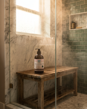 Bottle of soap on a wooden shelf in a bathroom with green tiles.