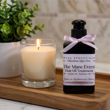 A bottle of KDCC Essentials 'The Mane Event' hair oil treatment stands on a wooden tray next to a lit candle in a glass jar, with a potted green plant in the background.