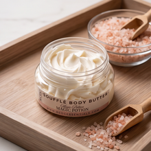 An open jar of ECG Essentials Soufflé Body Butter with creamy off-white cream, displayed on a wooden tray alongside pink Himalayan salt and a wooden scoop.