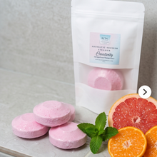 A white resealable pouch labeled RCDC Aromatic Shower Steamers Creativity Fragrance Treatment stands on a tiled surface with pink bath steams and citrus slices beside it.