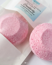Pink bath bomb and bath steamers in a clear resealable pouch with a white label reading 'ROMATIC SHOWER STEAMER Creativity (grapefruit tangerine)' and 'ROCKNROLLER ESSENTIALS'.