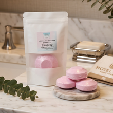 A white stand-up pouch labeled 'BTDG Aromatic Shower Steam Creativity' stands on a marble countertop beside three pink bath salts and a soap dish in a bathroom setting.