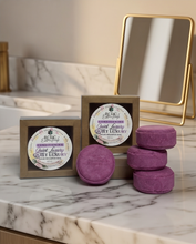 Three purple rectangular bath soaks in brown boxes and three matching round bath soaks on a white marble countertop, with a gold-framed mirror in the background. The labels read 'Scent of Beauty' and 'Quiet Luxury'.