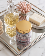 A jar of whipped soap scrub labeled 'Mermaid Dreams' sits on a mirrored tray beside a glass decanter, a bar of soap on a dish, and a coral decoration in a bathroom setting.
