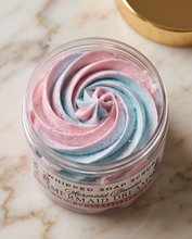 A clear jar of whipped soap scrub with pink and blue swirled cream and tiny glitter specks, labeled 'Mermaid Dream' by BCD Cosmetics, set on a light marble surface with a gold lid in the background.
