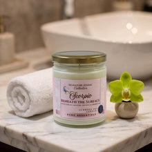 A jar candle labeled 'Scorpio Beneath the Surface' by Signature Zen & Co Collection, styled on a marble bathroom counter next to a rolled towel and a green orchid flower.