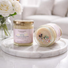 Two jars of scented candles on a marble surface with flowers in the background