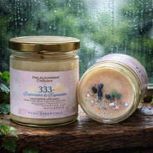 Two scented candles from The Alignment Collection on a wooden surface with a rainy window background.