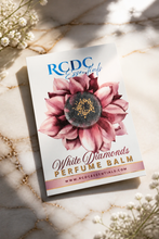 RCDC Essentials Diamonds Perfume Balm packaging card featuring a pink watercolor flower illustration, styled on a marble surface with dried flowers and soft shadows.